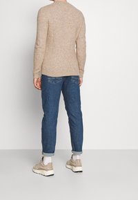 Maglione beige con una finitura texturizzata, jeans blu slim-fit e sneakers beige. Il maglione presenta maniche lunghe e un collo rotondo.