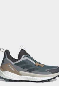 Donkergrijze en zwarte Adidas Terrex trail hardloopschoen met witte gevoerde zool en beige accenten, zijaanzicht op een effen lichte achtergrond.