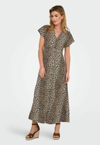 Robe maxi imprimée léopard avec manches courtes, décolleté en V et ourlet fluide. Fabriquée en tissu léger à la texture douce. Associée à des sandales compensées brunes.