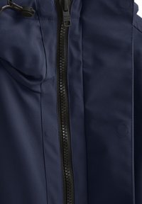 Giacca blu navy con zip centrale, texture liscia, cappuccio regolabile con coulisse e dettagli a bottone circolare sul tessuto.
