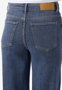 Κοντινή λήψη μπλε τζιν παντελονιού από πίσω με δύο πίσω τσέπες και μια καφέ ετικέτα στη ζώνη που λέει "NOISY MAY."