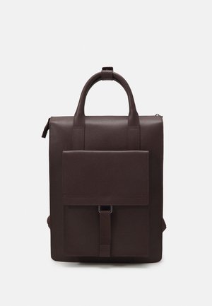 Tmavě hnědý kožený batoh s horním držadlem, klopou předního kapsy zabezpečenou popruhem a kovovou přezkou a zapínáním na zip na jednobarevném pozadí.