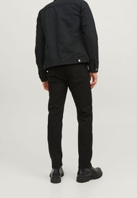 Chaqueta de lienzo negra con un diseño ajustado y detalles metálicos, combinada con pantalones negros ajustados y botines negros. 