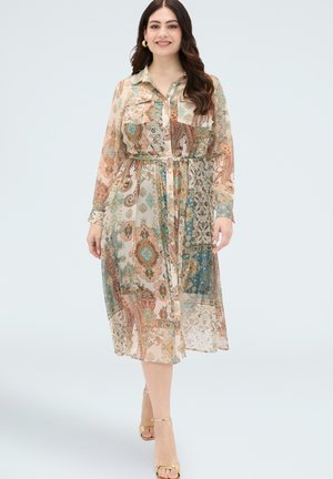 Frau geht, trägt ein langärmliges, geknöpftes, gemustertes Midikleid mit abstraktem Paisley-Design und goldenen offenen Zehenabsätzen.