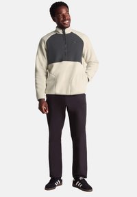 White fleece pullover with gray front panel, half-zip collar, and side pockets. Paired with black pants and dark shoes.