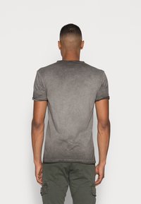 Camiseta gris de manga corta con un diseño en degradado, textura suave y dobladillos cosidos. Llevada con pantalones cargo en color verde oliva.