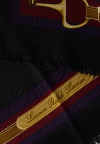 Sort stof med gentaget mønster af ridningselementer og et bånd med "Lauren Ralph Lauren" i gyldne bogstaver. Kanter er frynsete.