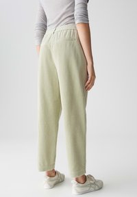 Pantaloni in velluto a coste verde chiaro con vestibilità comoda, dotati di una cintura elastica, tasche laterali e un motivo testurizzato discreto.