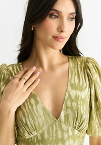 Green dress with a v-neckline, puff sleeves, and a textured pattern. Accented with subtle metallic threads, showcasing a soft, flowing fabric.