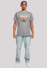 Grå bomull t-skjorte med et fargerikt "Scooby-Doo!" grafisk trykk. Kombinert med lyseblå jeans og hvite joggesko.