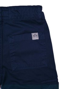 Navy blue kangashorts, joissa on sivutasku ja kudottu merkki, jossa on kirjainyhdistelmä 'B/R' ristikkäisten työkalujen designillä. Matte pinta.