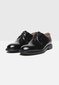 Zwarte leren dresschoenen met een glanzende afwerking, ronde neus, vetersluiting en contrasterende stiksels op de zool. Gladde textuur.