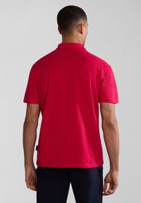 Červené polo tričko, krátké rukávy, jednobarevná tkanina, design límce, pohled zezadu, štítek na dolní levé straně, kombinováno s tmavými kalhotami.