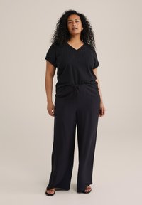 Čierne tričko s v-neck výstrihom a krátkymi rukávmi, zdobené textúrovaným vzorom, v kombinácii s voľnými čiernymi nohavicami s nastaviteľným šnúrkovým pásom.