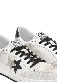 Sneakers bianche in pelle con lacci neri, dotati di accenti di stelle nere e argentate, punta strutturata e adesivo per il tallone nero.