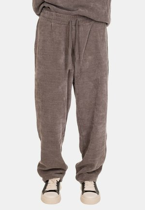 Pantaloni da jogging grigi a costine con cintura elastica, cordino e tasche laterali. Abbinati a scarpe da ginnastica chiare con dettagli neri.