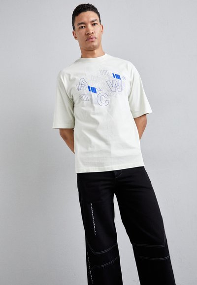 Lys grøn kortærmet t-shirt med blå geometriske grafikker. Kombineret med sorte bukser, der har hvid syning og tekstdetaljer.