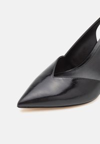 Zapato de tacón negro de piel con diseño slingback y punta afilada, que presenta un corte en V profundo, textura suave y una silueta minimalista y elegante.