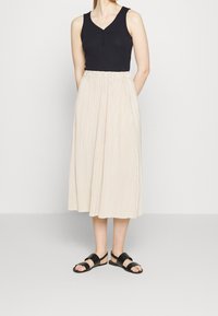 Black tank top with v-neck and buttons, paired with a knee-length, pleated beige skirt and black flat sandals. Smooth fabric textures.