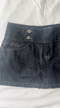 Tmavomodrá džínsová sukňa s priliehavým pásom, dvoma striebornými gombíkmi a pútkami na opasok. Obsahuje predné vrecká a kontrastné šitie.