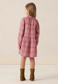 Langärmliges pinkes Kleid mit floralem Muster, rüschigem Kragen und elastischen Manschetten. Gezeigt mit braunen Wildleder-Stiefeletten. Rückansicht dargestellt.