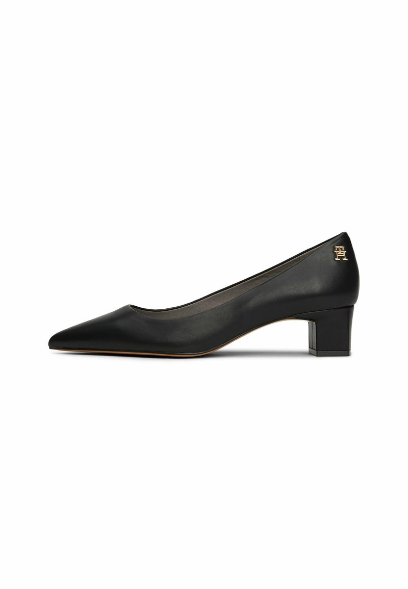 Chaussure pour femme en cuir noir avec un petit talon carré, bout pointu et petit logo doré près du talon.