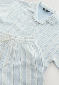 Light blue and white knit polo shirt with buttons and matching drawstring pants featuring a vertical zigzag and stripe pattern.
