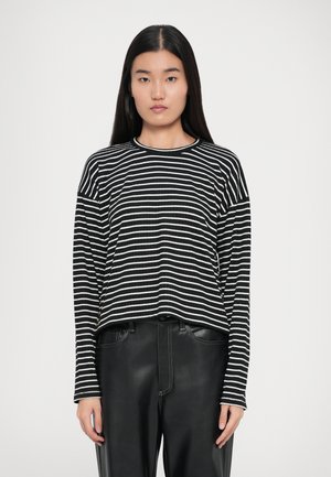 Chemise rayée noir et blanc à manches longues en rib ou avec un col rond, présentant des épaules tombantes et une coupe décontractée. Associée à un pantalon noir brillant.