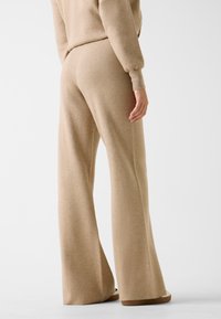 Beżowe dzianinowe spodnie o szerokich nogawkach mają luźny krój i teksturowaną powierzchnię, z wysokim paskiem i subtelnymi detalami przeszyć dla dodatkowego stylu.