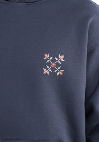 Sweat-shirt bleu marine à texture douce, avec un petit motif floral en crème clair et rose sur la poitrine gauche.