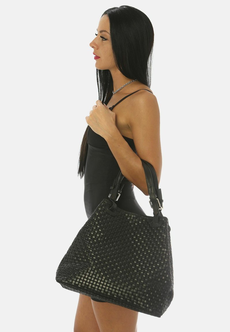 Mustan kudotun käsilaukun joka on muodoltaan strukturoidun, jossa on kaksinkertaiset kahvat ja sileä tekstuuri. Koristeina hopeiset yksityiskohdat ja ompelutiedot.