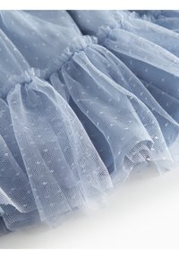 Tessuto di tulle blu chiaro con ruffle arricciati, caratterizzato da piccole pois bianchi. Texture morbida e trasparente con un aspetto fluido e a strati.