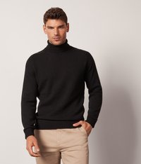 Schwarzer Rollkragenpullover aus Strickstoff, mit einem gerippten Kragen und Bündchen. Getragen mit hellbeigen Hosen.