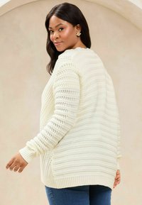 Helle elfenbeinfarbene Strickjacke mit horizontalen und vertikalen Streifenmustern, strukturiertem Garn und langen Ärmeln mit gerippten Bündchen.