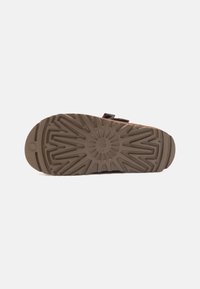 Bruine rubberen sandaalzool met een gestructureerd patroon, voorzien van groeven voor grip en een afgeronde teentop, met versterkte randen.