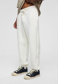 Witte sweatpants met een trekkoord in de taille, gemaakt van zachte stof; gedragen met zwarte sneakers met beige accenten en veters.