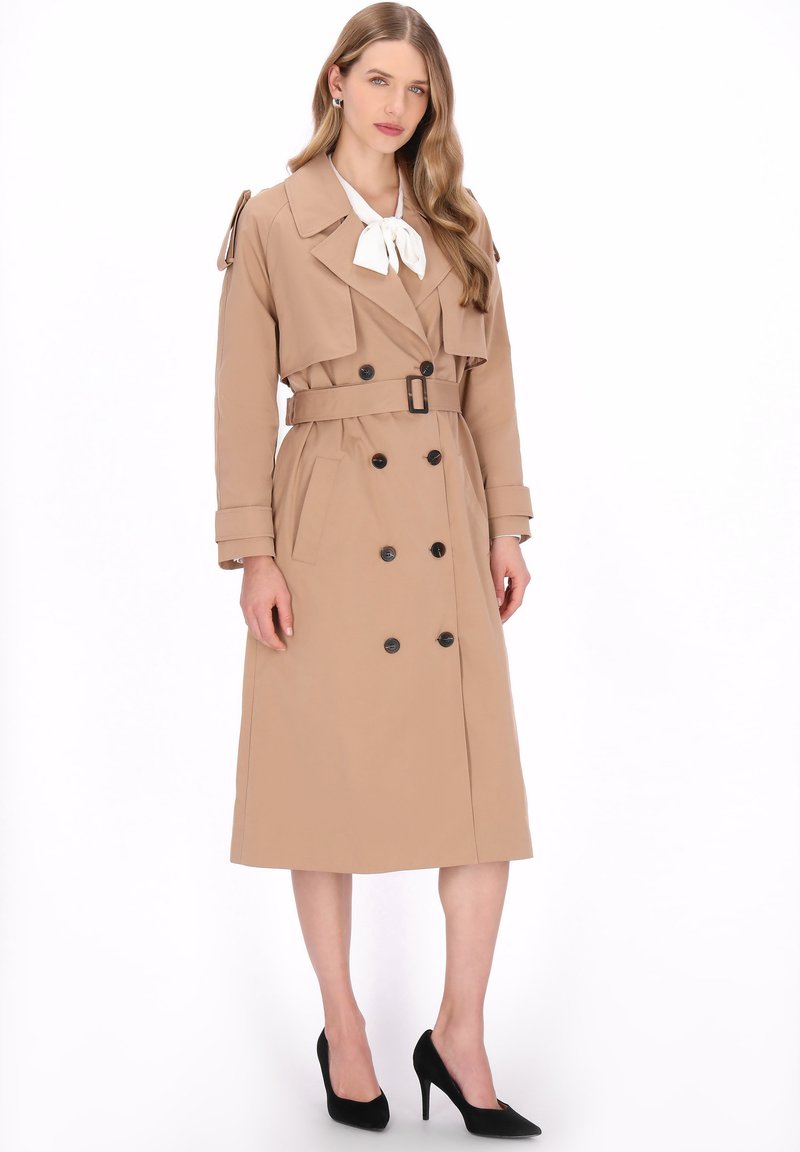Beiger Trenchcoat mit doppelreihiger Knopfleiste, tailliertem Gürtel, weitem Kragen und Schulterakzenten. Glatte Textur, knielang.