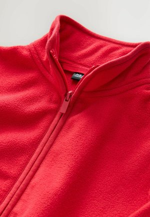 Punainen fleece-takki, jossa on korkea kaulus, täyspitkä vetoketju ja pehmeä teksturoitu kangas. Sisäkauluksessa on ripustustagi.