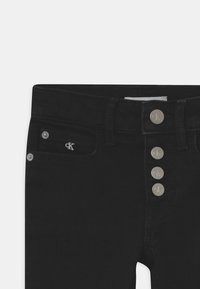 Jeans de mezclilla negra con cierre de cinco botones, bolsillos frontales y un sutil logo bordado. Textura suave con un ajuste clásico.