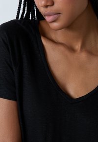 T-shirt nera con scollo a V, maniche corte, realizzata in tessuto leggero. Primo piano sul collo e sulla spalla, che mette in evidenza una texture liscia.