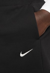 Fekete sportnadrág, puha textúrával, elöl fehér Nike swoosh logóval és kényelmes, elasztikus derékkal.