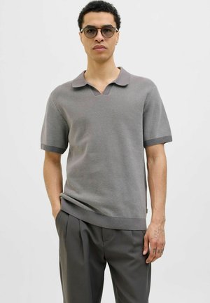 Tricou polo tricotat gri, cu decolteu în V, mâneci scurte și manșete ribbate. Purtați cu pantaloni gri, evidențiind o suprafață texturată.