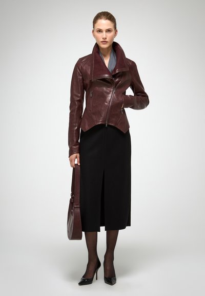 Veste en cuir bourgogne avec fermeture éclair asymétrique, large col et ourlet angulaire ; associée à une jupe midi noire et des escarpins pointus.