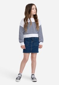 Prugasta bela in mornarsko modra pletena majica z rebrastimi manšeti, skupaj z modrim jeans krilom. Črne in bele športne copate dopolnjujejo obleko.