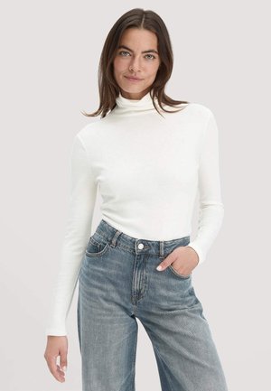 Weißes Langarm-Turtleneck-Shirt aus weichem Stoff, kombiniert mit hellblauen, hoch taillierten, weit geschnittenen Jeans. Einfaches, klares Design.