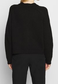 Černý pletený svetr s kulatým výstřihem, dlouhými rukávy a žebrovaným lemem. Texturovaná tkanina s volným střihem, zobrazeno zezadu.