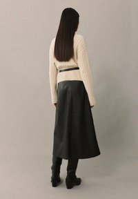 Pulover bej cu model în relief, asociat cu o fustă midi din piele neagră, prinsă în talie, având o textură netedă și cizme negre până la glezne.