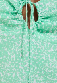 Mint green fabric with a white floral pattern, featuring a gathered texture and a center keyhole opening secured with ties.