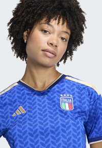 Italy home soccer jersey in blue, featuring a leaf pattern, gold accents, a round collar, and the national emblem with stars on the chest.