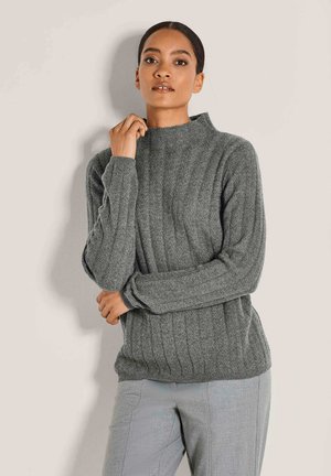 Grijze gebreide trui met een hoge kraag, voorzien van een gestructureerd ribpatroon en lange mouwen. Gecombineerd met lichtgrijze broek.